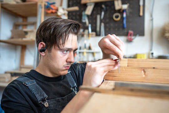 Concentrated professional man restorer making measurements of patch on vintage window frame at table, professional crafter using ruler and marking dimensions and size with pencil on wooden frame board