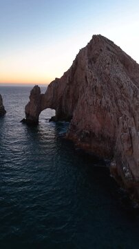 Vertical drone shot of the Arch of Cabo San Lucas cliff at dusk over calm ocean water in Mexico