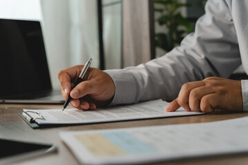 Obraz na płótnie Canvas Business person reviewing a printed document with a pen on a clipboard beside a laptop, showing an office document checking process for paperwork verification and administrative review.