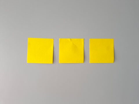 Three blank yellow sticky notes arranged in a row on a gray surface 