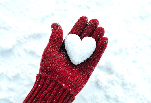 Heartshaped snowball carefully held in a red woolen mitten on snowy ground