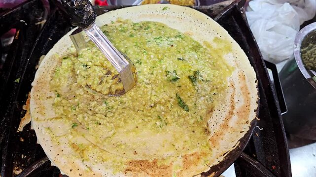 Close up of a street vendor mashing and spreading spicy potato masala across a crispy dosa on a hot tawa while preparing a popular South Indian dish at an Indian food stall