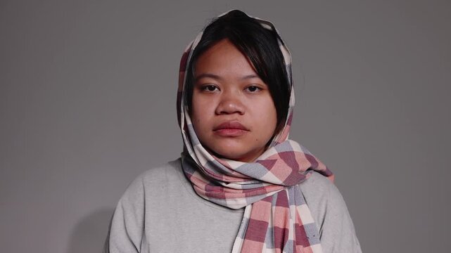 Portrait of a serious young Asian woman wearing a traditional checkered scarf wrapped around her head.
