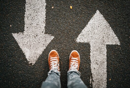 Person's feet standing between two white painted arrows on a paved road, pointing opposite directions