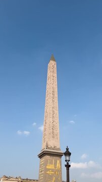 Luxor Obelisk rises above Place de la Concorde beneath clear blue Paris sky, vertical establishing