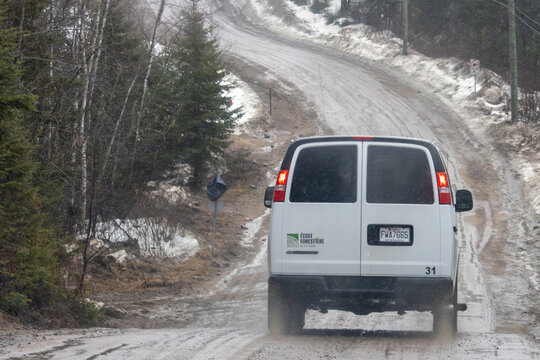 Canada, 13 April 2026 : White van with Ecole Forestiere de La Tuque logo drives on a muddy snowy road in a forest