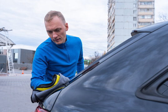 Concept of vehicle maintenance, wiping drying polishing car care cleanliness, modern contactless automated washing self services. Man cleans exterior of luxury car with microfiber rags. Automotive