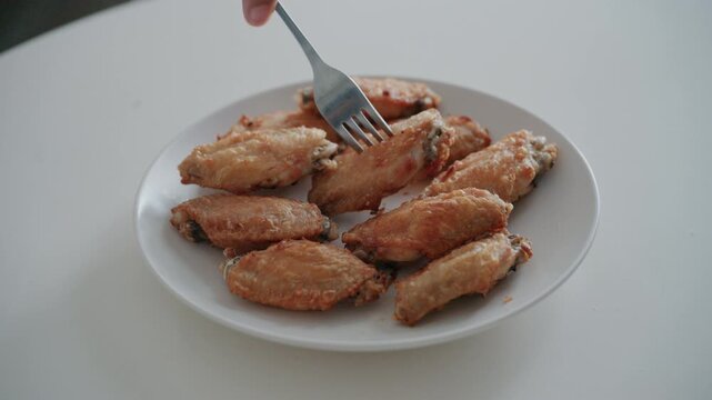 Person using fork to take delicious crispy fried chicken wing close up.