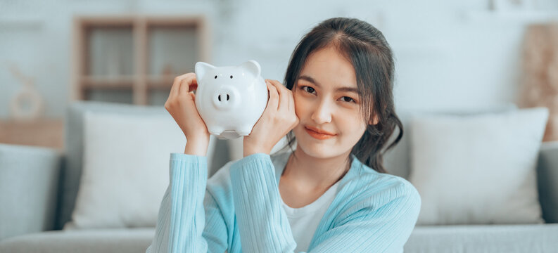 Young Asian woman holding piggy bank and sitting on the floor at home. Save money and financial investment