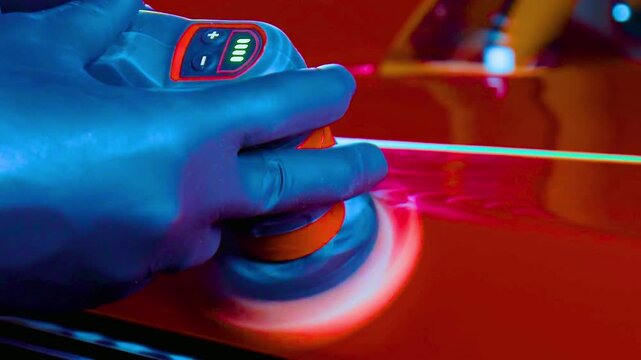 Gloved hands using rotary polisher on red car body under studio light