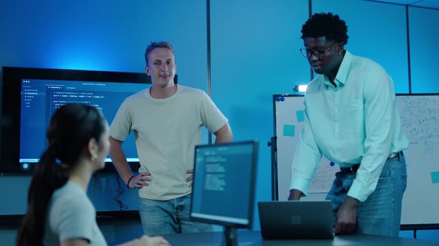 Diverse team of software developers working together in a modern tech office with blue lighting. IT programmers collaborating on code analysis, cybersecurity, and software engineering projects.
