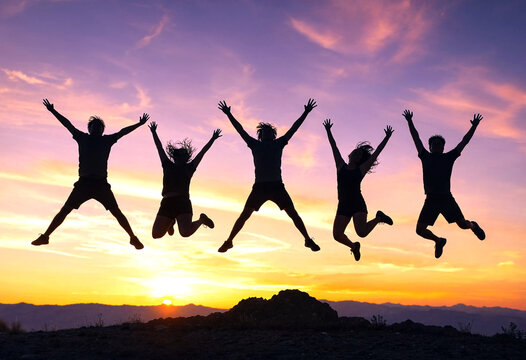 Group of happy friends jumping at sunset with arms raised enjoying freedom and adventure together outdoors