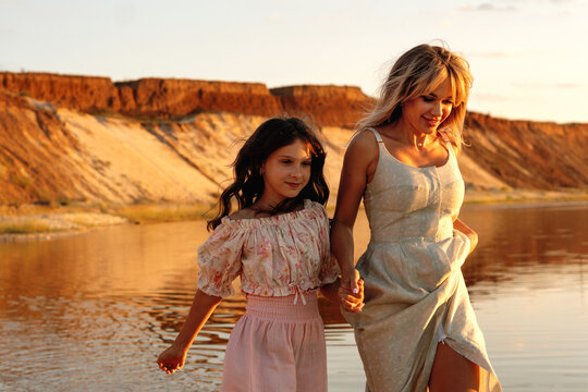 Mother And Daughter Walking Together Beside Sunset Water