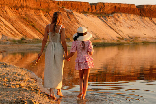 Mother And Daughter Walking Into Lake At Sunset