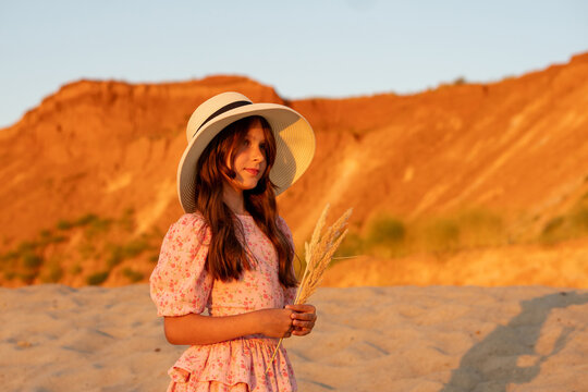 Girl Holding Dry Reeds Before Sunlit Cliffs