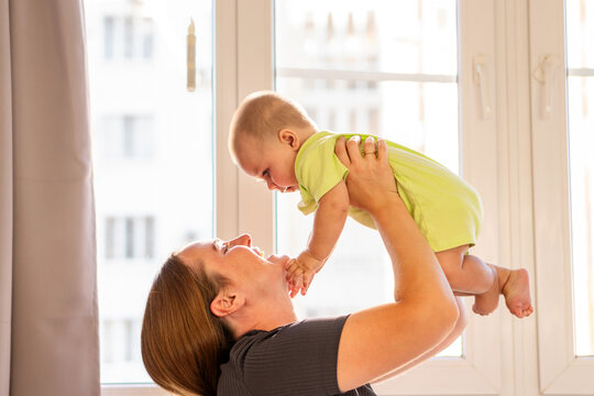 Baby Boy Reaches Toward Mother While Lifted Near Window
