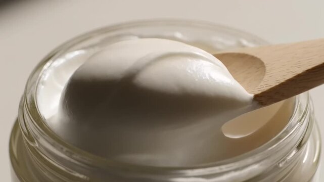 Close-up of a wooden spoon scooping creamy white yogurt from a glass jar, showcasing the smooth texture and rich consistency of the dairy product.
