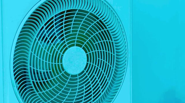 Air conditioning unit fan spinning behind teal plastic grill outdoor