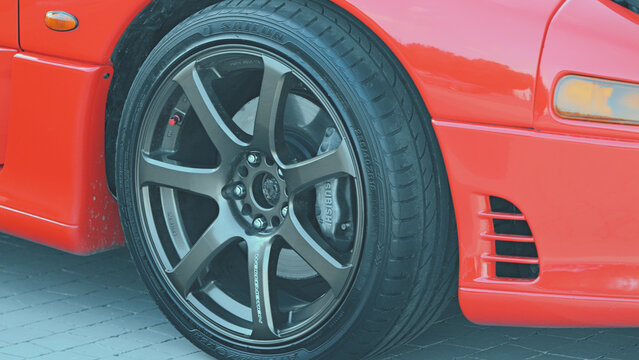 Closeup of red sports car wheel featuring black multi spoke rim, performance tire, visible brake caliper. Bright daylight highlights glossy paint metallic textures. Krasnodar, Russia. July 10, 2025