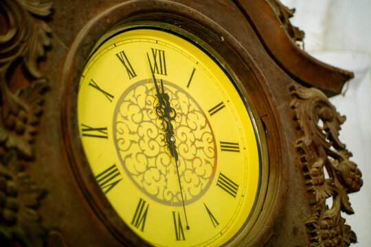 Vintage carved wooden wall clock with yellow face and roman numerals showing twelve o clock