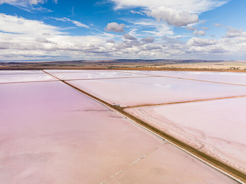 Aerial view of Bumbunga Lake with pink salt water pools separated by earthen embankments under a blue sky with scattered clouds in Wakefield Regional Council, South Australia, Australia.