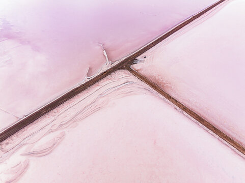 Aerial view of the vibrant pink waters of Bumbunga Lake, featuring salt crust patterns and intersecting causeways in Wakefield Regional Council, South Australia, Australia.