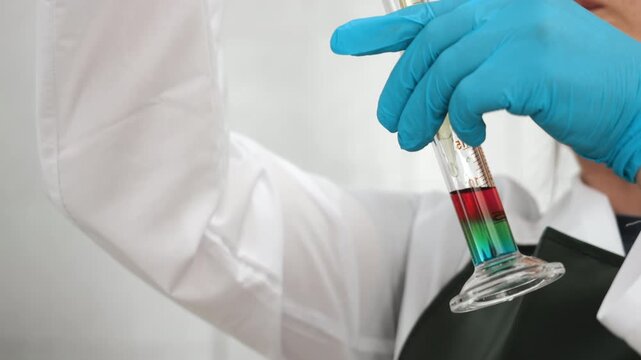 Laboratory scientist examines separated layers of colored liquids in a graduated glass cylinder during chemical analysis, testing and scientific research.