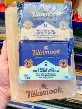 A hand holding a Tillamook Farmers' Collection cheese gift pack with two cheddar blocks on a wooden board - August 08, 2026 Tillamook Oregon, USA