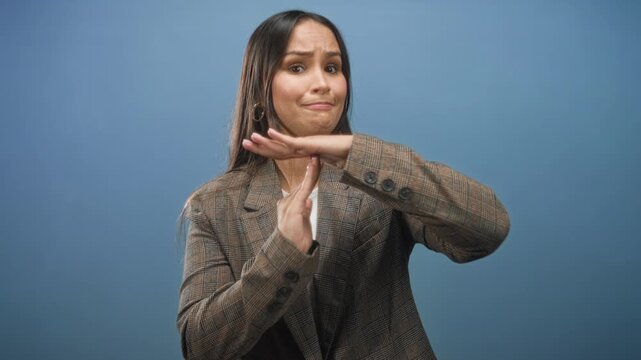 Woman in checked blazer making timeout hand gesture with palms and fingers visible in studio blue backdrop and neutral lighting; skepticism.