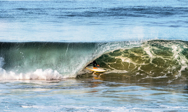 Surfer rides inside a powerful ocean wave barrel, catching the light