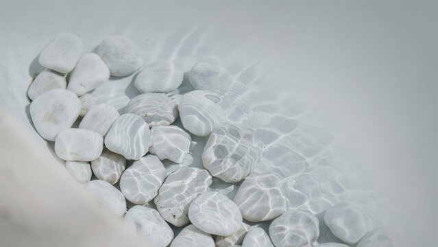 Smooth white river stones resting underwater in a clear basin with rippling light patterns dancing across the surface of the submerged rocks