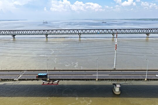 Aerial view of Jamuna Bridge spanning the Jamuna River with a vehicle on the road deck and power lines overhead in Tangail District, Dhaka Division, Bangladesh.