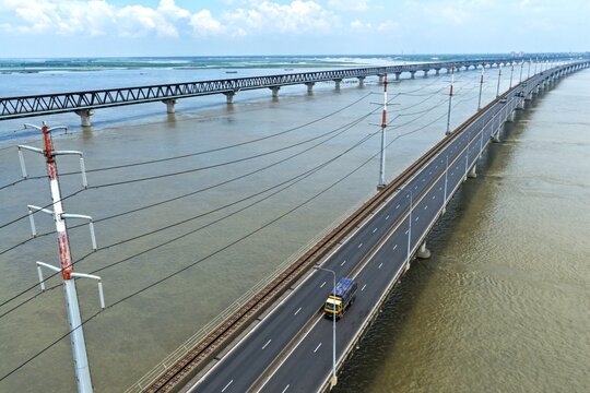 Aerial view of Jamuna Bridge spanning the Jamuna River with a truck driving on the road and power lines alongside in Tangail District, Dhaka Division, Bangladesh.