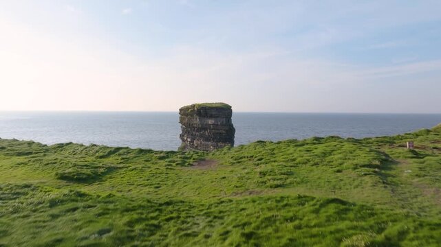 Camera glides over green clifftop grass to reveal the isolated Dun Briste sea column rising from open water.