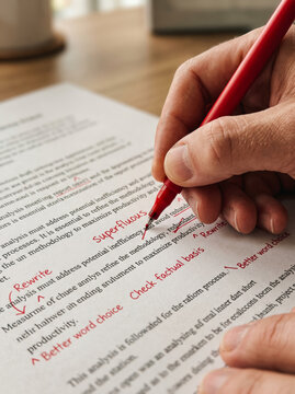 Close Up Hand Correcting and Marking Text Document with Red Pen at Office Desk