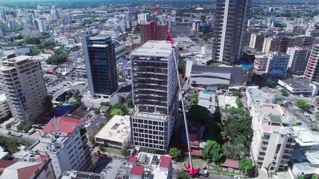 igh-angle aerial drone tracking shot pulling back and orbiting right over a modern skyscraper under construction with a large crane crane in Naco, Santo Domingo