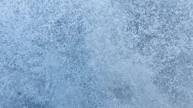Dense microbubbles rising through pale blue liquid, forming vertical streams, clustering into soft foam, and creating lively aerated texture with shimmering highlights