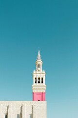 Obraz premium Historic ornate bell tower with pink accents rising above a stone cathedral facade against a clear blue sky for European heritage tourism branding