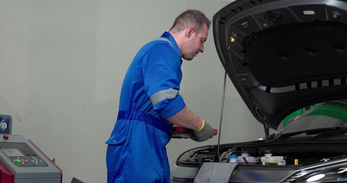Mechanic using tester to check electric vehicle EV battery voltage under open hood in garage