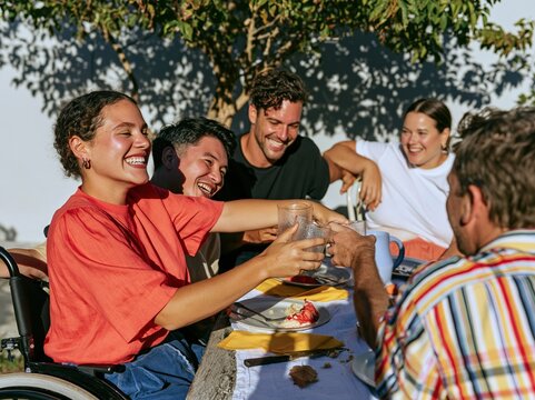 Diverse group of friends toasting at a garden birthday gathering with a woman in a wheelchair, featuring glowing amber light for lifestyle and community concepts
