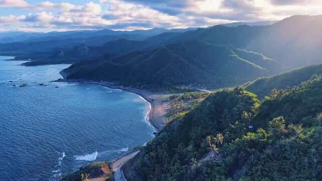 Cinematic aerial drone video of a winding coastal road nestled between lush green mountains and deep blue ocean. Beautiful pristine sandy beach at sunrise golden hour. Epic nature travel landscape.