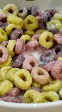 Close up view of a spoon stirring colorful breakfast cereal loops in a white bowl with milk. Nutritious and sweet kid's morning meal