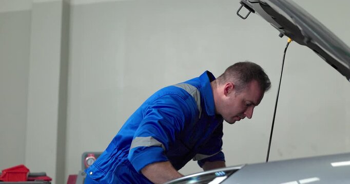 Mechanic using tester to check electric vehicle EV battery voltage under open hood in garage