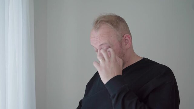 Middle aged man squints and rubs tired eyes while staring closely at a smartphone, showing digital eye strain from heavy screen use.