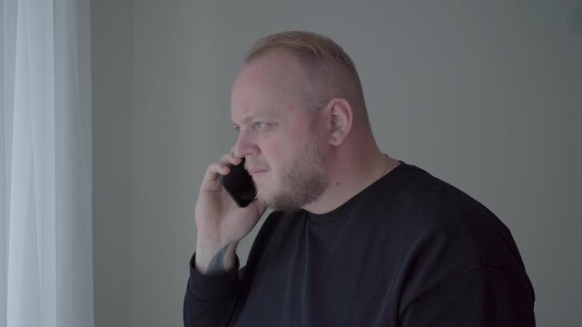 Bearded man in a dark sweater listens to a troubling phone call, frowning as he suspects AI voice cloning fraud.