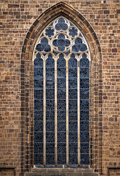 Window with vintage glass panes. Window in traditional European brick architecture. Historic Gothic window on old exterior. Medieval church window with pointed arches.