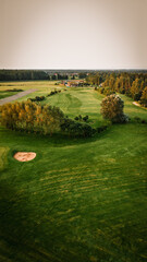 Fototapeta premium Aerial view of a lush green golf course with manicured fairways, sand traps, and trees under a clear sky, showcasing the serene landscape of a recreational area