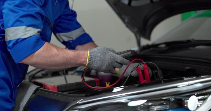 Mechanic using tester to check electric vehicle EV battery voltage under open hood in garage