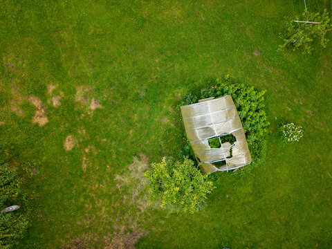 Aerial view of a damaged greenhouse with a torn plastic roof situated in a lush green field in Andrioniskis, Utena County, Lithuania.