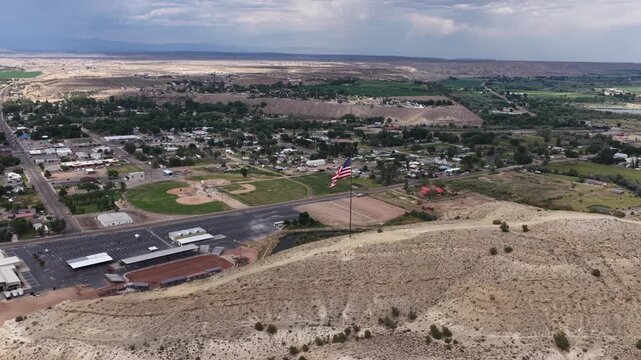 Aerial of American flag in Duchesne Utah on desert hillside with stormy sky above residential area
